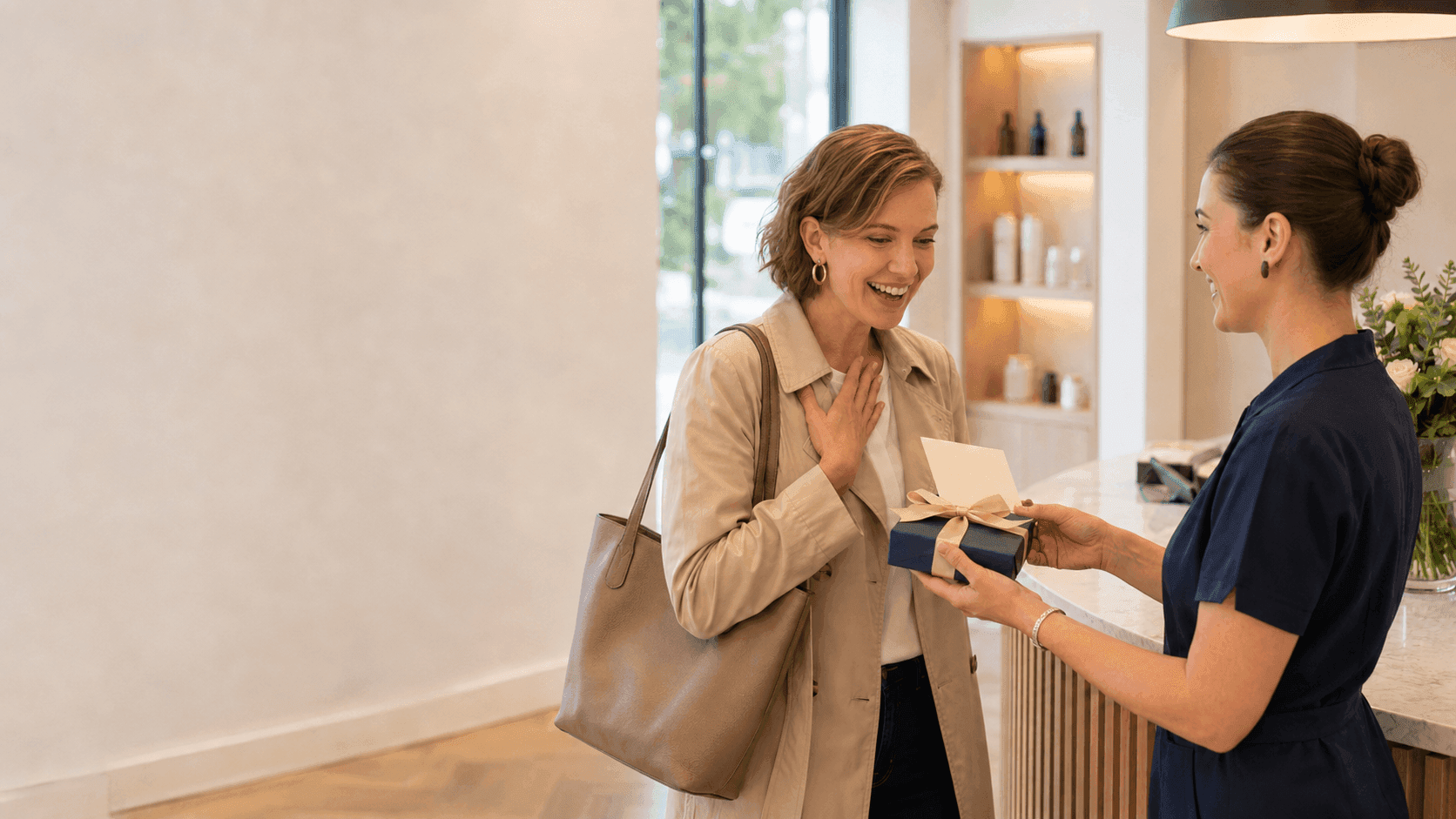 Smiling woman in trench coat receives a small blue gift from a staff member.