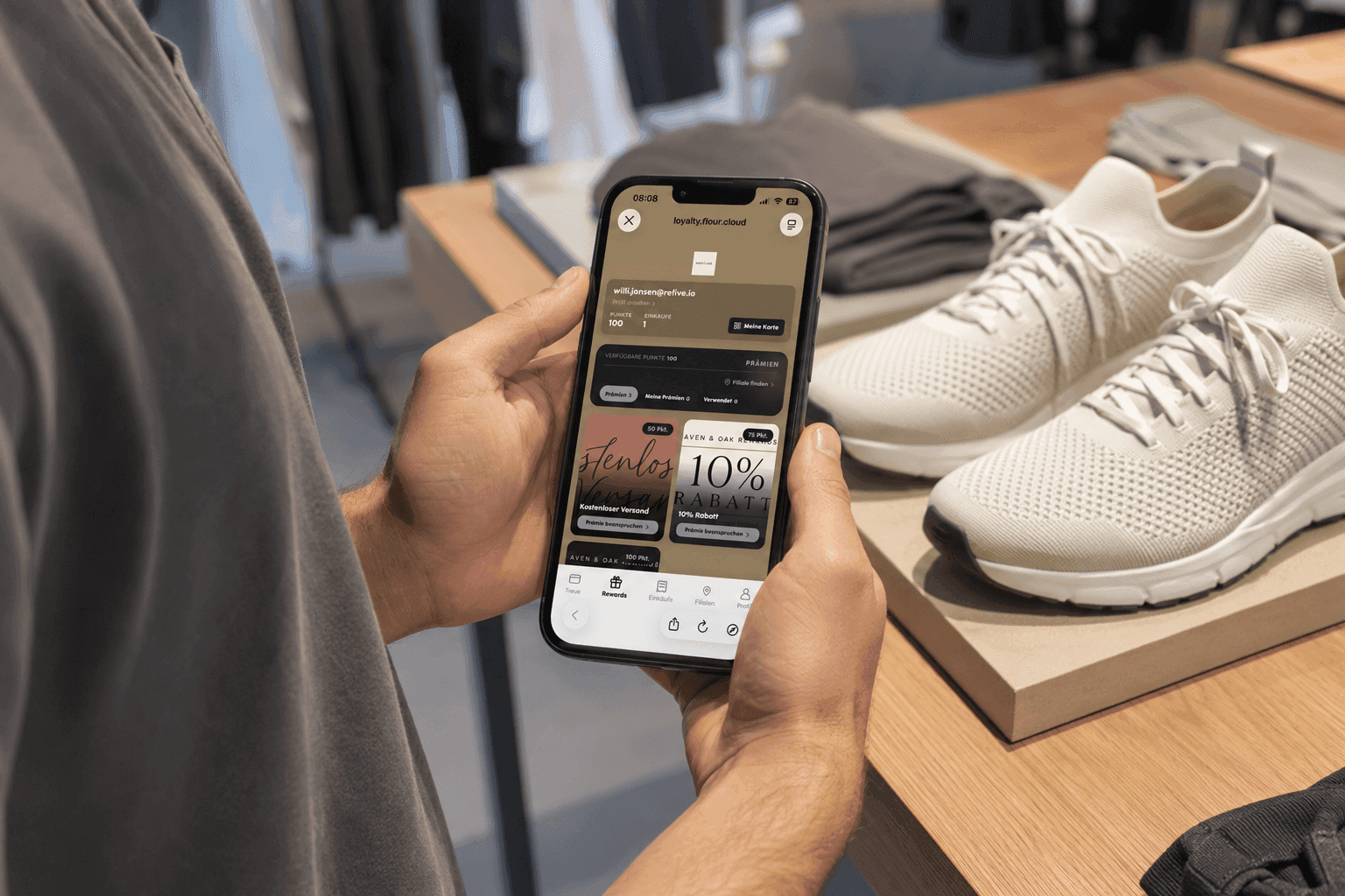 Person holds a smartphone displaying a shopping app in a retail store with sneakers.